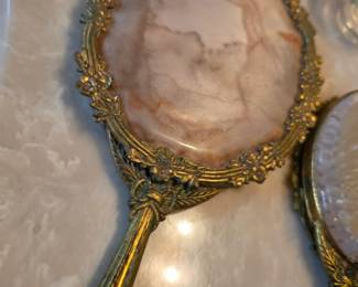 Ornate vintage vanity mirror featuring an intricate gold-tone frame and decorative stone-look design. Discover unique vintage accessories, home décor, and collectible treasures at this Tavares, FL estate sale by Kinfolk Estate Sales.