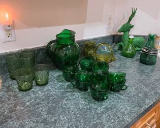 Collection of vintage green glassware including a matching pitcher, tumblers, mugs, decorative bottles, and serving pieces. Beautiful collectible glassware and entertaining essentials available at this Tavares, Florida estate sale hosted by Kinfolk Estate Sales.