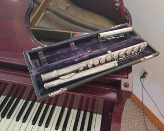 Baby grand piano displayed with a silver concert flute in its original case. Featured musical instruments at this Tavares, Florida estate sale, along with quality furniture, home décor, and unique collectibles from Kinfolk Estate Sales.