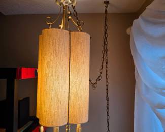 vintage mid-century modern hanging swag lamp features a textured, woven cylindrical fabric barrel shade with decorative gold trim and fringe