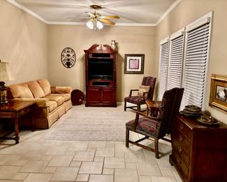 Traditional three-cushion sofa features a warm caramel velvet upholstery and classic skirted base , single drawer end table featuring  classic turned legs and a polished warm finish, TV Armoire , Lamp, wall art, accent table with open lower storage shelf, dark wood accent chair , area rug 