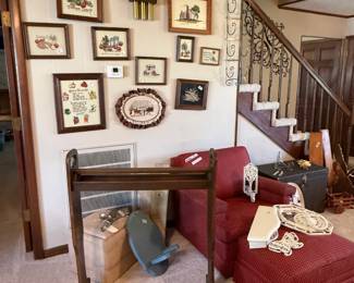 So many framed cross stitch pieces.  Old wood quilt rack and good soft chair with matching ottoman.
