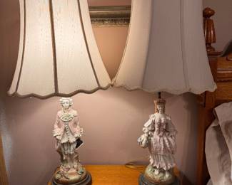 Pair of vintage MCM Italian porcelain figural table lamps features hand-painted 18th-century style aristocratic court or colonial couple figurines set on dark circular bases with scalloped fabric shades. Approx. 35h x 7" w base. $