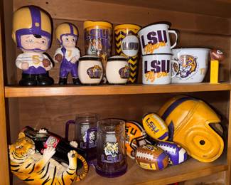 LSU ITEMS: Top Shelf, Left to Right: Vintage Ceramic Big-Head Football Player Bank/Figurine, $20. Vintage Ceramic Football Player Figurine, $15. LSU Tigers Insulated Travel Tumblers, $5 each. LSU Ceramic Salt & Pepper Shakers, $10.  White Ceramic LSU Tigers Mugs & Serving Bowl Set, $20. Novelty Football Pez Dispenser, $3. Bottom Row, Left to Right: Ceramic Tiger Wine/Coke Bottle Holder, $10. National Championship Coca-Cola Bottle, $12. Heavy Glass LSU Beer Steins (pair), $15. Mini LSU Replica Helmet & Soft Footballs, $3 each. Vintage Golden-Yellow Leather Football Helmet, 1940's era, $45. 