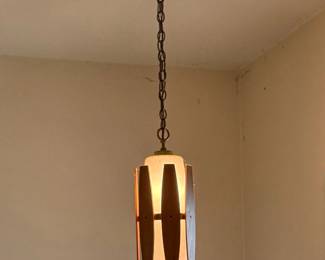 A mid-century modern hanging pendant light features a cylindrical frosted glass accented with vertical wooden slats.