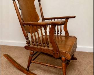 Antique wooden platform rocking chair with high back, turned spindles, decorative side rails, and carved/pressed detailing. Solid, substantial construction with a warm aged finish. Researched prior to sale.