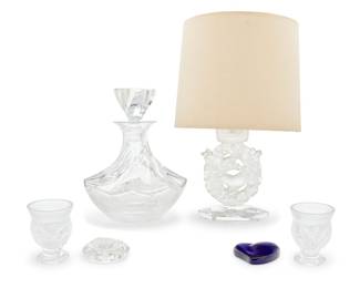 1164 Five Lalique glass table items Late 20th/early 21st century Each etched to underside: Lalique ® France Comprising a 'Mesanges' lamp, 'Aberdeen Swirl' decanter, pair of 'Saint Cloud' cigarette urns, and maple leaf paperweight, together with a Tiffany cobalt glass cordiform paperweight by Elsa Peretti 6 pieces Lamp overall height with shade 13 1/2 in., diameter 9 in.; height of decanter 9 3/4 in., diameter 7 in. Estimate: $500 - $700