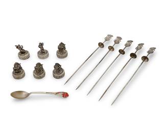 1226 A collection of Southeast Asian silvered metal and sterling objects 20th century Each place card holder marked: CAMBODGE / T900; spoon marked: STERLING Comprising one Bangkok commemorative sterling silver and enamel spoon, six silvered metal figural place card holders, and five silvered metal skewers with figural handles 12 pieces Length of skewers 9 1/8 in.; height of place card holders 2 in. Weighable sterling 0.4 gross oz. troy approximately Estimate: $200 - $400