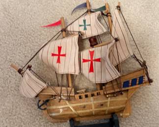 wooden model of the Santa María, Christopher Columbus's famous 1492 flagship, featuring striped fabric sails marked with red and green crosses and a small decorative anchor mounted on a black stand