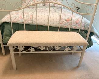 cream-cushioned white metal scrollwork bed bench features a decorative floral and leaf motif along the front apron rail