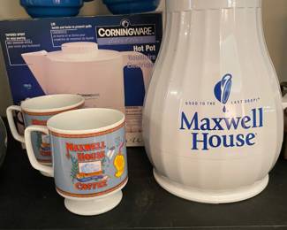 collection of vintage Maxwell House promotional merchandise, including blue stacking mugs, a white thermal insulated carafe pitcher, and a Corningware Electrics Hot Pot box