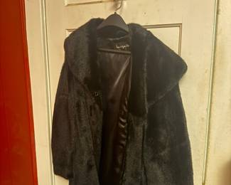 Black leather jacket with fur collar hanging on closet door