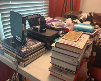 Desk workspace with stacked books, papers, magazines, and collectibles