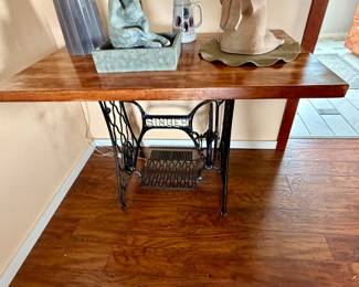 custom console table featuring a polished wooden top mounted on an antique black cast-iron Singer sewing machine treadle base with a white logo accent