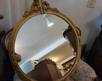 Ornate round gold-gilt wall mirror, featuring a Rococo-style crest, with a decorative wooden frame