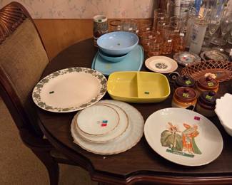 Same table with a yellow divided serving dish, decorative plates including one with an oriental figural design, and a blue lidded dish.