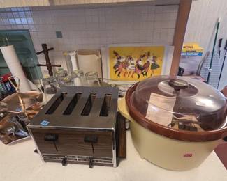 Vintage General Electric four-slice toaster in chrome and woodgrain, beside a Rival Crock-Pot slow cooker in harvest gold with brown trim and clear dome lid. A Polish folk dancer serving tray, glass tumblers, and Pyrex mixing bowls in yellow and green are visible nearby.