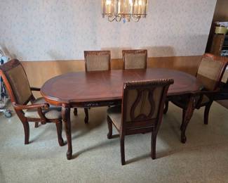 Oval wood dining table with a leaf, surrounded by six cane-back captain's chairs, set beneath a crystal chandelier.