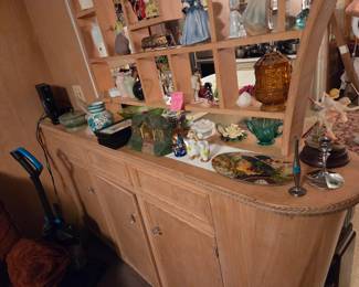 Blonde wood buffet with a lattice-back top shelf and cabinet doors below, topped with an assortment of decorative glassware.