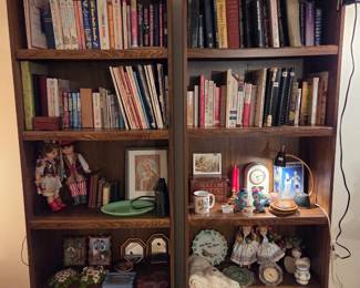 Wood bookshelf filled with books, collectible clocks, decorative plates, and small figurines.
