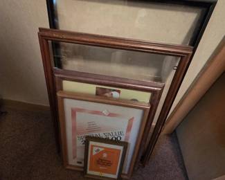 Assortment of picture frames in a range of sizes, including a large black metal frame, oak and walnut-finish wood frames, and smaller document frames still in original retail wrap.