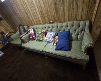 Vintage French Provincial style sofa with carved fruitwood frame, cabriole legs, and tufted back in sage green brocade, paired with a matching armchair. Topped with handmade granny-square crochet pillows, a gingerbread man plush, and a boxed animated Swinging Santa figure.