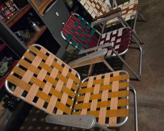 Vintage aluminum folding lawn chairs with woven webbing in orange and multicolor patterns.