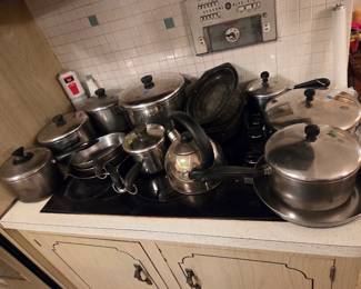 Assortment of stainless steel cookware including pots, pans, and a tea kettle, grouped on the stovetop.
