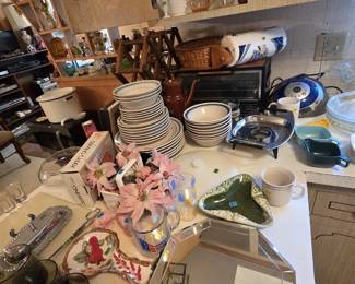 Kitchen counter stacked with a blue-banded stoneware dish service including dinner plates, salad plates, and bowls, plus a brown drip coffee pot, a toaster oven, a Coby CD clock radio, an octagonal beveled mirror tray, a green ceramic ashtray, and milk glass pieces on the upper shelf.