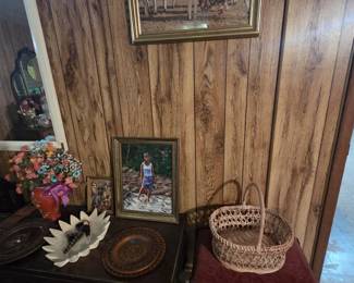 Polish folk art grouping featuring a framed print of highlander folk dancers in traditional dress, a Black Madonna of Czestochowa icon, a carved wooden plate, an original painting of a girl wading a stream, a woven wicker basket, and a small upholstered footstool atop a vintage cabinet.