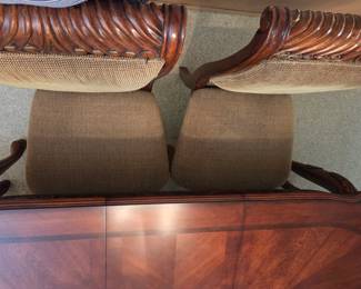 Detail of a pair of dining chairs with rope-twist carved wood crest rails and woven cane backs, paired with a glossy wood table.