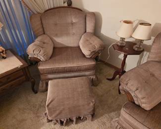 Pair of matching tufted wingback armchairs with a skirted ottoman, flanking a small wood side table with two lamps.