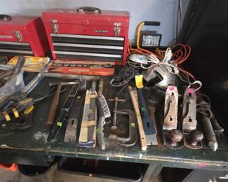 Two red Craftsman multi-drawer tool chests with a Fleetwood 40-piece tap and die set in original box, two vintage Stanley bench planes, C-clamps, wire brushes, files, hammers, a halogen work light, trouble light, and extension cords on a workbench.