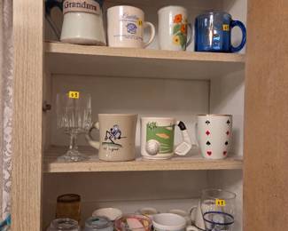 Cabinet shelves filled with a collection of decorative coffee mugs, including one reading Grandma.