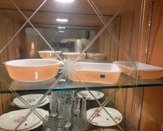 Top shelf of the same cabinet holding a set of vintage pink mixing bowls and casserole dishes.