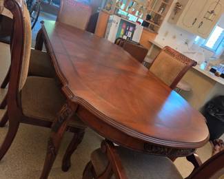 Oval dining table with rope-twist carved chairs, shown in an open kitchen and dining area with light cabinetry and a chandelier.