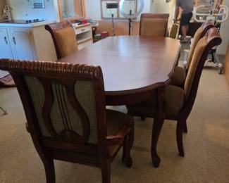 Wider view of the same oval dining table and cane-back chairs, showing the open kitchen and breakfast nook beyond.