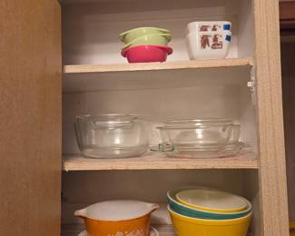 Kitchen cabinet with vintage glass bakeware and mixing bowls, including an orange floral-pattern casserole dish.