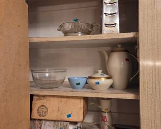 Cabinet shelf with mixing bowls, a ceramic pitcher, and a small wood box, with additional glassware on the shelf below.