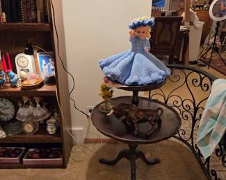Wrought iron round side table, shown with a crocheted doll figure on top and a shelf of collectible figurines nearby.