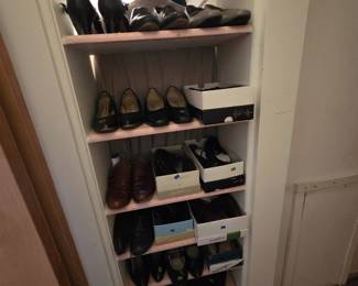 Built-in closet shelving stocked with ladies dress shoes, primarily black leather pumps and flats with some brown leather pairs, including boxed pairs from Easy Spirit and other makers.