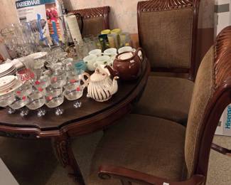 Dark wood side table with cane-back chairs, topped with assorted glassware and a decorative shell figurine.