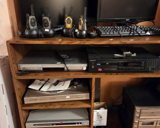 Wood shelving unit with a computer monitor and keyboard, cordless phones, and stacked DVD players.