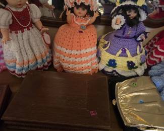 Three handmade crochet-dressed bed dolls with ruffled gowns and matching bonnets in peach, lavender with flower trim, and red and white with pearl necklace. Also shown are a footed wooden display stand and a gold lame evening clutch.