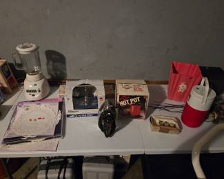 Small kitchen appliances including a blender, a boxed Hot Pot beverage warmer, a clothes iron, and a red water cooler jug.