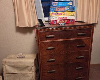 Tall wood chest of five drawers, topped with a stack of board games.