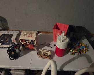 Same table with the boxed Hot Pot, clothes iron, and water cooler jug, shown from another angle with an artificial floral arrangement.