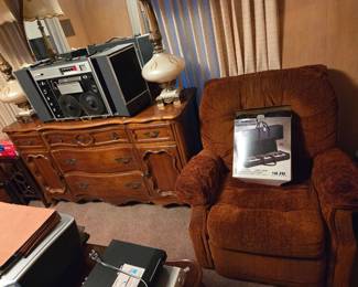 Vintage component stereo system with built-in speakers on the dresser, next to a brown recliner with a boxed item on the seat.