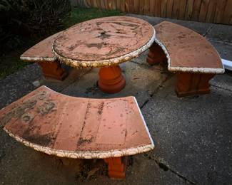 Weathered concrete outdoor patio set with a round table and two curved benches, terra cotta finish.