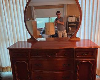 Wood dresser with an attached oval mirror, featuring six drawers in a French provincial style.